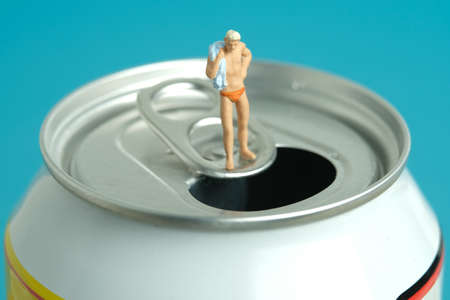 Miniature people toy figure photography. Creative summer vacation concept. A men standing above soft drink canned getting ready to swim. Image photoの写真素材