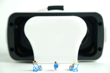Miniature people toy figure photography. Virtual travel concept, group of men and girl relaxing seat while watching in front of goggles device, isolated on white background. Image photoの写真素材
