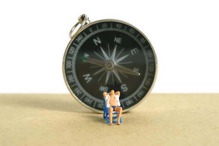 Miniature people toy figure photography. Travel destination, Men relaxing at beach chair with black compass, isolated on white background. Image photoの写真素材