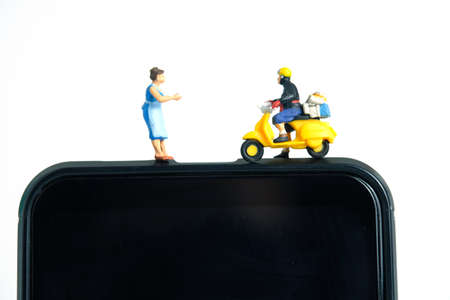 Miniature people toys conceptual photography. Mobile post service delivery. Postman courier standing above smartphone, isolated on white background.の写真素材