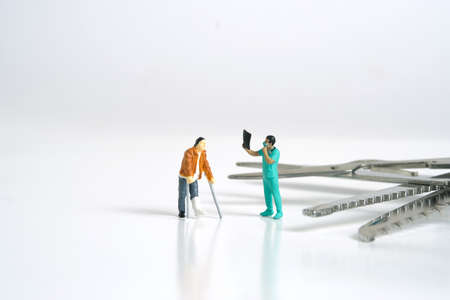 Miniature people toy figure photography. A men broken bones with doctor looking on X-ray results with surgical equipment, isolated on white background. Image photoの写真素材