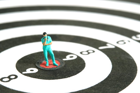 Miniature people toy figure photography. A men doctor or nurse thinking in the middle dartboard target. Image photoの写真素材