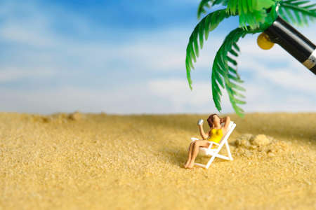 Miniature people toy figure photography. A girl relaxing on beach chair drinking a soft drink under the coconut tree. Image photoの写真素材