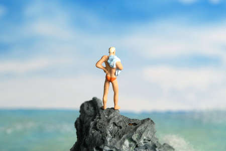 Miniature people toy figure photography. A men standing at a rock getting on beach ready to do cliff jump. Image photoの写真素材
