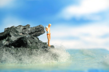 Miniature people toy figure photography. A men standing at a rock getting on beach ready to do cliff jump. Image photoの写真素材