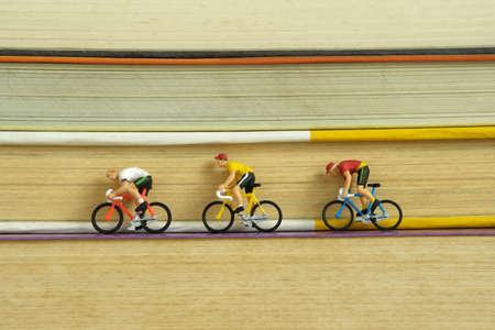 Miniature people toy figure photography. Creative concept. A biker cycling above book stack. Image photoの写真素材