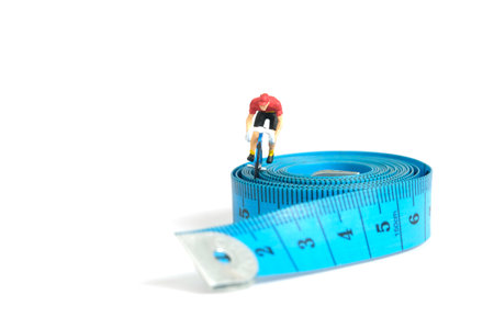 Miniature people toy figure photography. Fat burn concept. A biker cycling above measure tape, isolated on white background. Image photoの写真素材