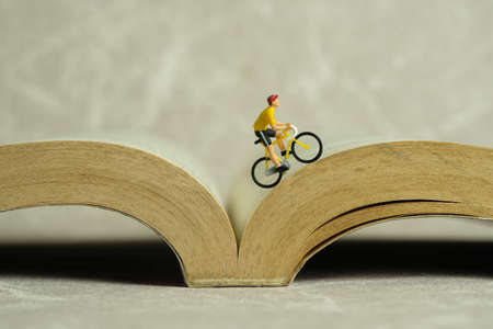 Miniature people toy figure photography. Creative concept. A biker cycling above book opened. Image photoの写真素材