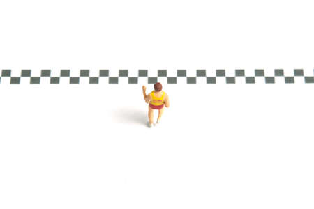 Miniature people toy figure photography. A fat man running towards the finish line, isolated on white background. Image photoの写真素材