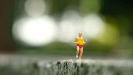 Miniature people toy figure photography. Solo jogging. A fat men running at park outdoor track. Image photoの写真素材