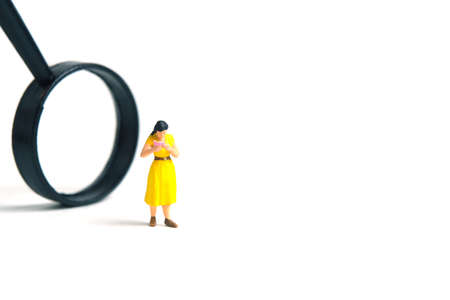 Miniature people toy figure photography. A girl student standing beside magnifier glass, isolated on white background. Image photoの写真素材
