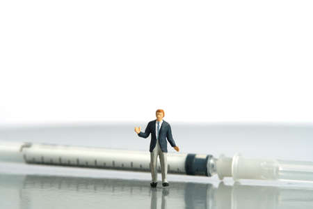 Miniature people toy figure photography. Hesitation on vaccination concept. A shrugging businessman standing in front of syringe vaccine. Isolated on white background. Image photoの写真素材