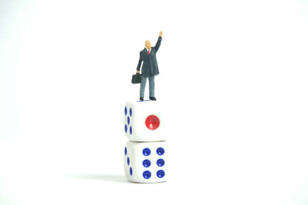 Miniature people toy figure photography. A businessman standing above dice stack while raise his...