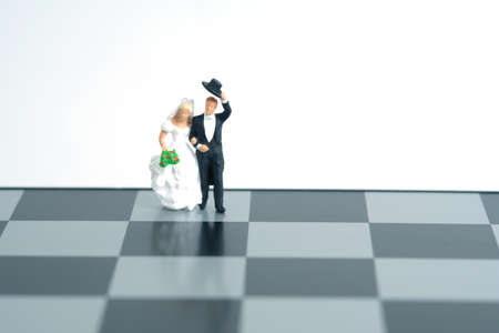 Wedding marriage strategy plan concept miniature people, toys photography. Bride and groom standing above chessboard isolated on white background. Image photoの写真素材