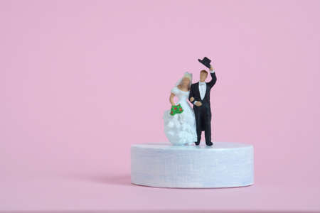 Wedding celebration concept miniature people, toys photography. Bride and groom standing above podium platform isolated on pink background. Image photoの写真素材