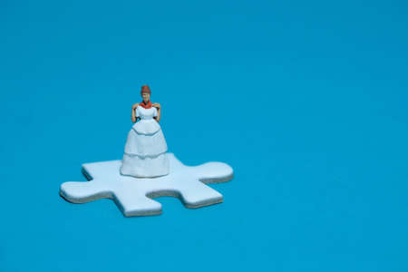 Wedding dress alternative. Miniature people women standing above puzzle jigsaw on blue background. Image photoの写真素材
