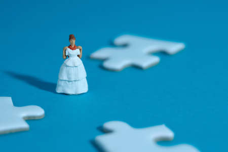 Wedding dress alternative. Miniature people women standing in the middle of puzzle jigsaw on blue background. Image photoの写真素材