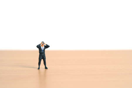 Businessmen standing using binoculars above wooden table. Miniature tiny people toys photography.の写真素材