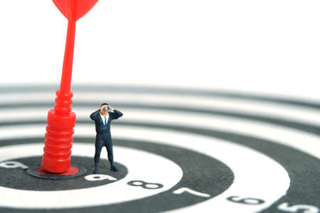 Businessmen standing above red arrow on dartboard using binoculars. Miniature tiny people toys photography. isolated on white background.の写真素材