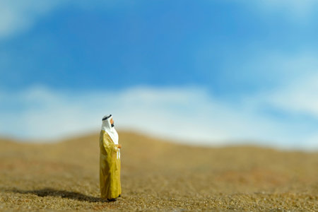 Miniature people toy figure photography. A Sultan wearing yellow bihst, king cloak, standing at desert in bright sky. Image photoの写真素材