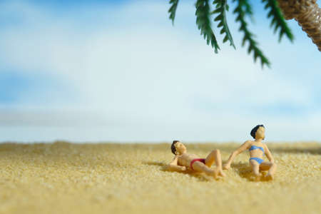 Miniature people toy figure photography. Men and girl couple relaxing, lying at beach sand when daylight at seaside. Image photoの写真素材
