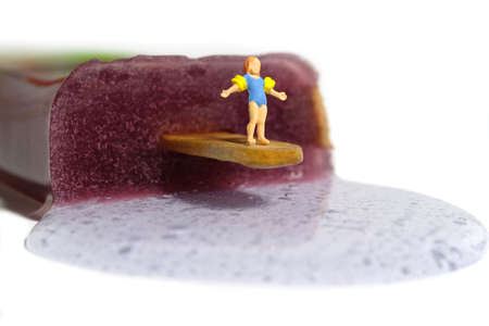 Miniature people toy figure photography. Creative summer vacation concept. A girl child with arm buoy standing above melting ice cream stick ready to swim. Image photoの写真素材