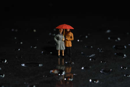 Miniature people toy figure photography. A couple using umbrella, walking on the floor full of...