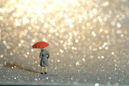 Miniature people toy figure photography. A lady wearing raincoat and umbrella, standing enjoying...