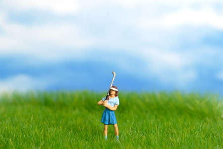 Miniature people toy figure photography. A girl golfer standing at meadow golf field on bright...