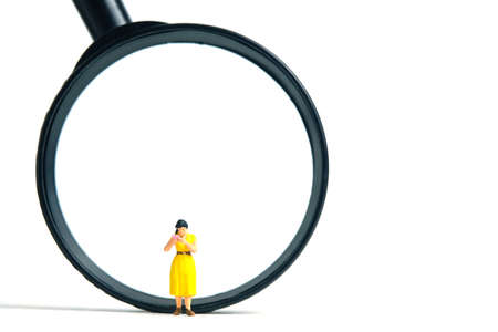 Miniature people toy figure photography. A women student standing in front of magnifier glass, isolated on white background. Image photoの写真素材