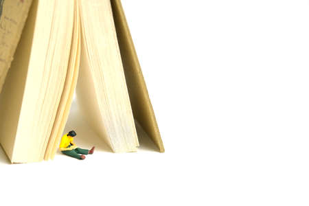 Miniature people toy figure photography. A men student sitting under book tent, isolated on white...