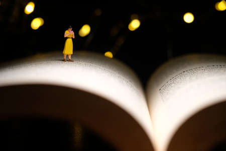 Miniature people toy figure photography. A girl reading a book at night with bokeh defocused light lamp, bed time routine before sleep. Image photoの写真素材
