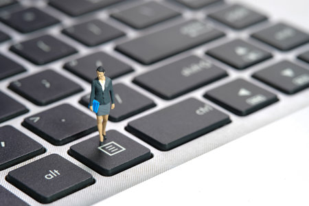 Miniature people toy figure photography. A businesswoman standing above notebook laptop keyboard....