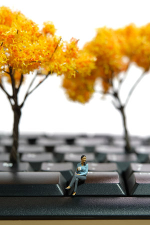 Miniature people toy figure photography. Coffee break concept. A businesswoman sitting above keyboard holding a cup of coffee tea on workplace at autumnの写真素材