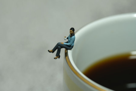 Miniature people toy figure photography. Coffee break concept. A businesswoman sitting above a cup of coffee tea on workplace. Image photoの写真素材