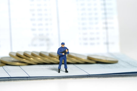 Miniature people toy figure photography. Bank account protection concept. A security officer standing above bank account with golden money coin. Isolated on white background. Image photoの写真素材