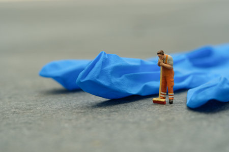 Miniature people toy figure photography. Tired sweeper cleaning worker standing in front of used...