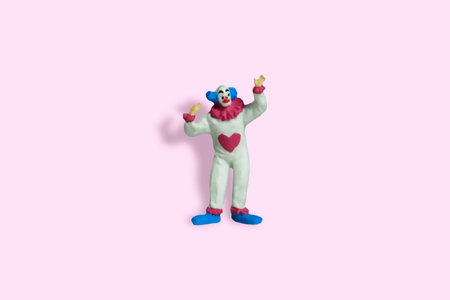 Miniature people toy figure photography. Front view of bald clown wearing white dress on pink pastel...