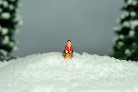 Miniature people toy figure photography. Winter holiday. A boy riding wooden sledge, sledding down the hill. Image photoの写真素材