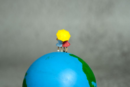 Miniature people toy figure photography. Two girls kid standing above earth globe. Grey cloudy background. Image photoの写真素材
