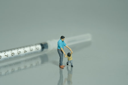 Miniature people toy figure photography. Refusing for injection concept. A father and son standing in front of needle syringe on grey background. Image photoの写真素材
