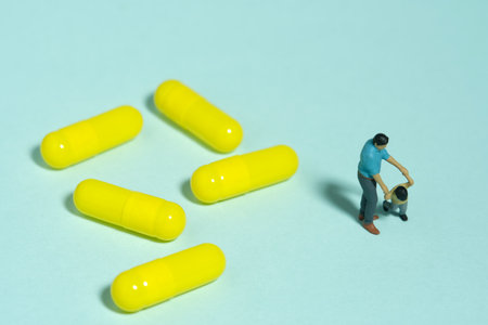 Miniature people toy figure photography. Drug medicine refuses concept. A father and son standing beside medicine pills. Isolated blue background. Image photoの写真素材