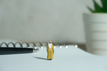 Miniature people toy figure photography. King Sultan standing above book in front of pen on a office desk. Image photoの写真素材