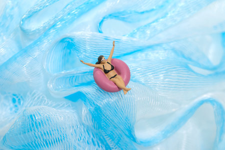 Miniature people toy figure photography. Girl wearing black sunglasses swimming with rubber tube ring on wavy ocean. Image photoの写真素材