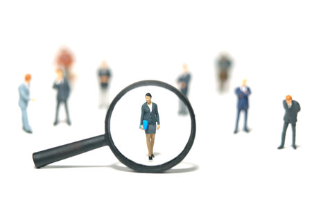 Miniature people toy figure photography. Women leader search. A businesswoman standing in the middle of male people crowd with magnifier glass. Isolated on white background. Image photoの写真素材