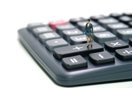 Miniature people toy figure photography. A businesswoman standing above calculator. Isolated on white background. Image photoの写真素材