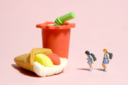 Miniature people toy figure photography. Healthy food eat and lunch break concept. Two girl kindergarten student standing in front of cake and soft drink. Isolated on pink background. Image photoの写真素材