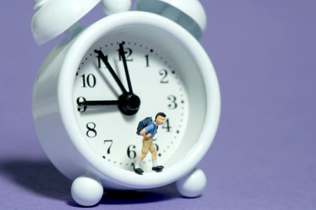 Miniature tiny people toy photography. A boy student with backpack standing on clock. Isolated on purple background. Image photoの写真素材
