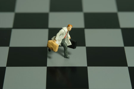 Miniature tiny people toy figure photography. A businessman running in the middle of chessboard carrying briefcase. Image photoの写真素材