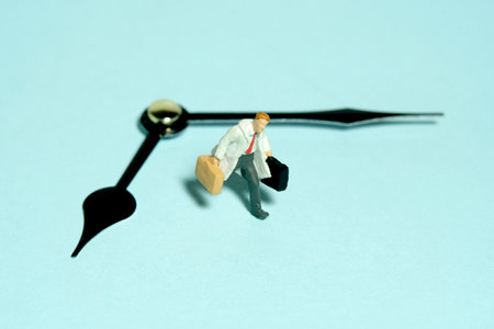 Miniature tiny people toy figure photography. A businessman running above black clockwise carrying briefcase. Isolated on blue background. Image photoの写真素材